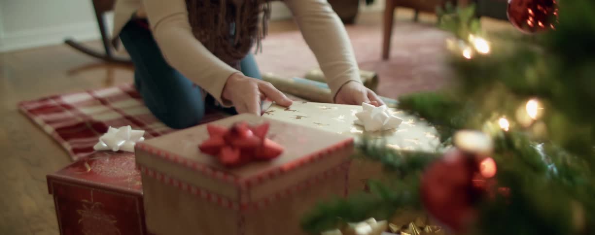 A woman placing a christmas gift underneath a christmas tree
