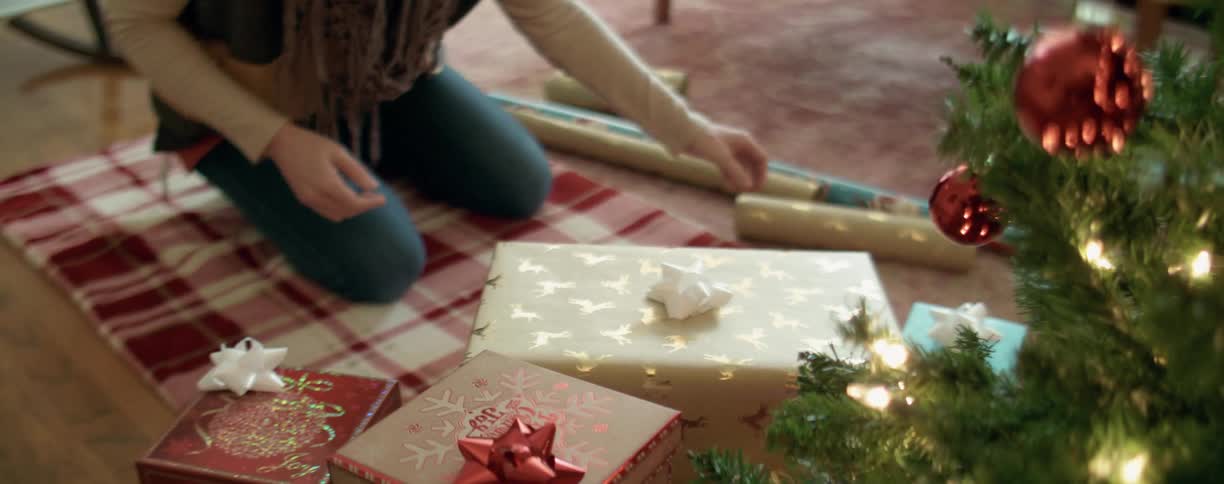 A woman places a wrapped gift under a christmas tree