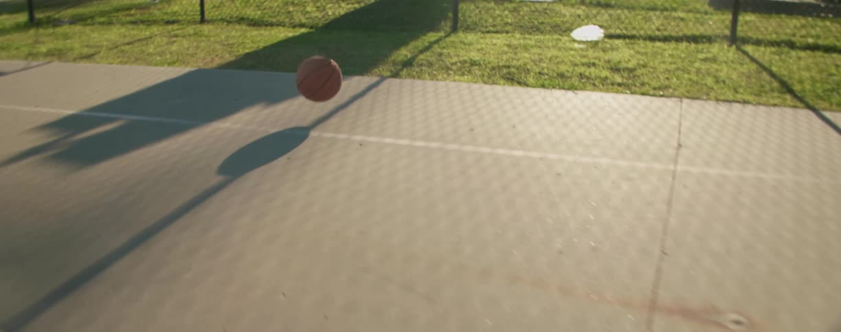 A basketball bouncing and rolling off the court onto grass