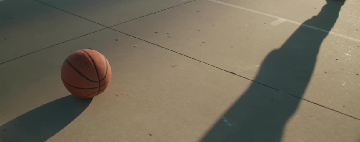 A basketball rollings on the cement flooring of an outdoor basketball court
