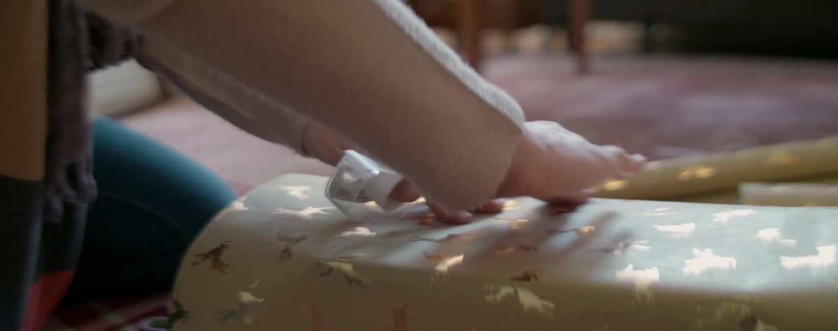 A white woman puts tape on a gift paper while wrapping a present