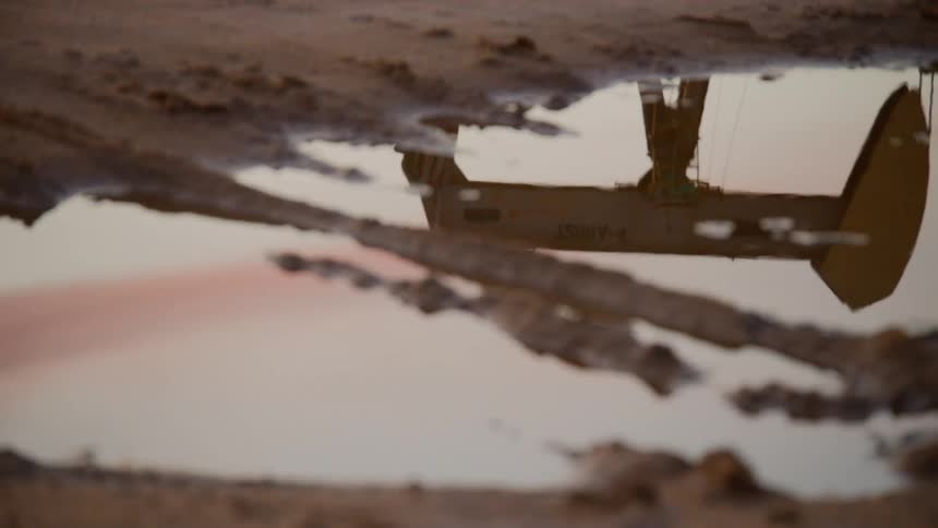 Puddle in muddy earth reflects sky and working oil pump