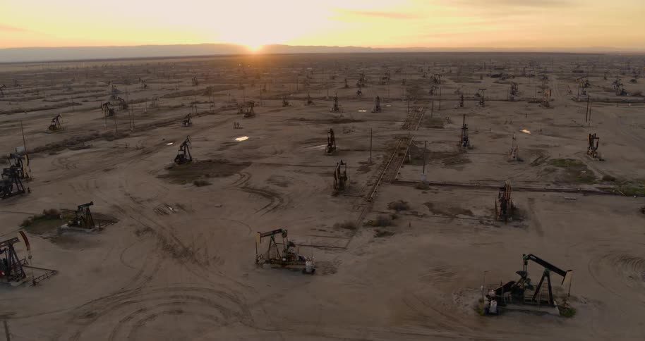Sun hovers on horizon near mountains as oil pumps occupy the desert