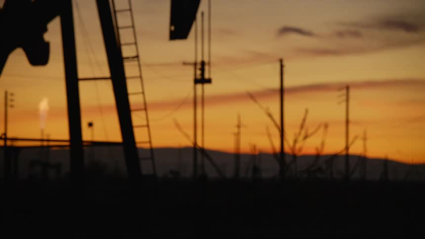 An oil drilling machine digs for oil in the field at sunset