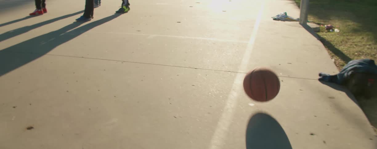 People standing on a basketball court as the ball rolls off the court onto grass