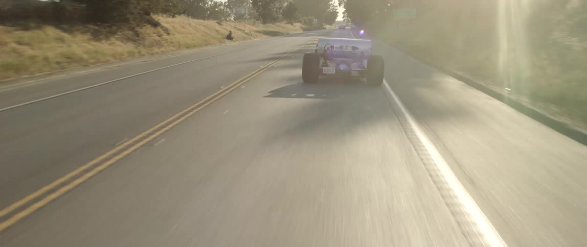 A race car drives down a road in a rural area