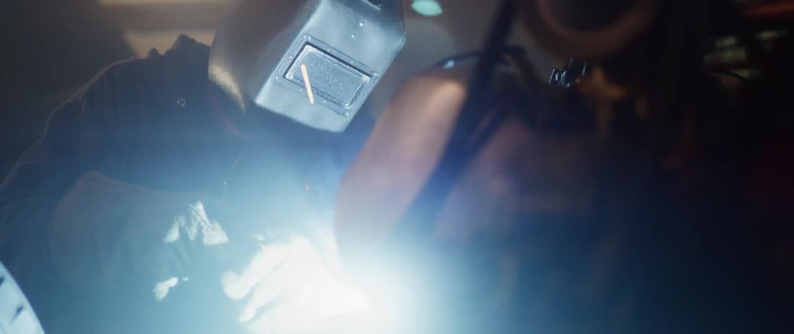 A person with a welding helmet and gloves welding