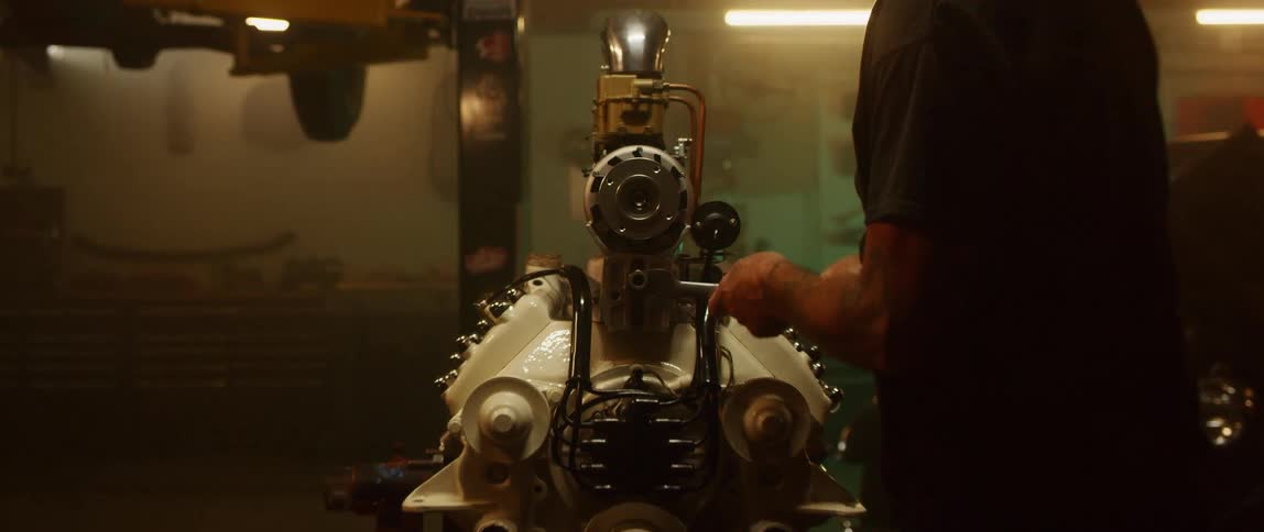 A white man turns a wrench on a car engine in a garage