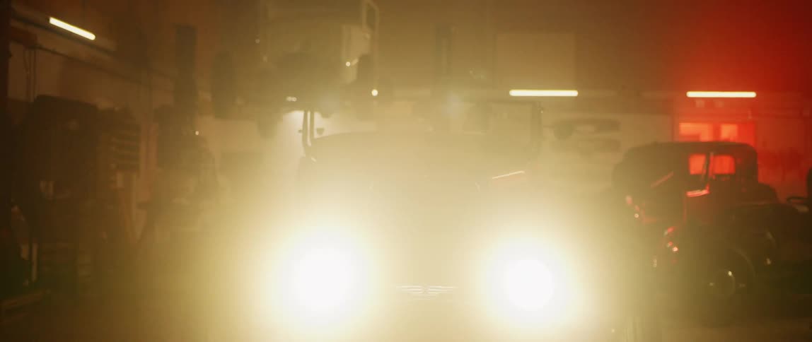 A man in a classic car in the garage turning on the headlights