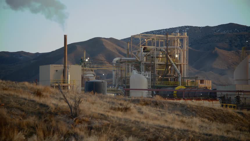 Smoke pours out from a smoke stack at an industrial spot near the mountains