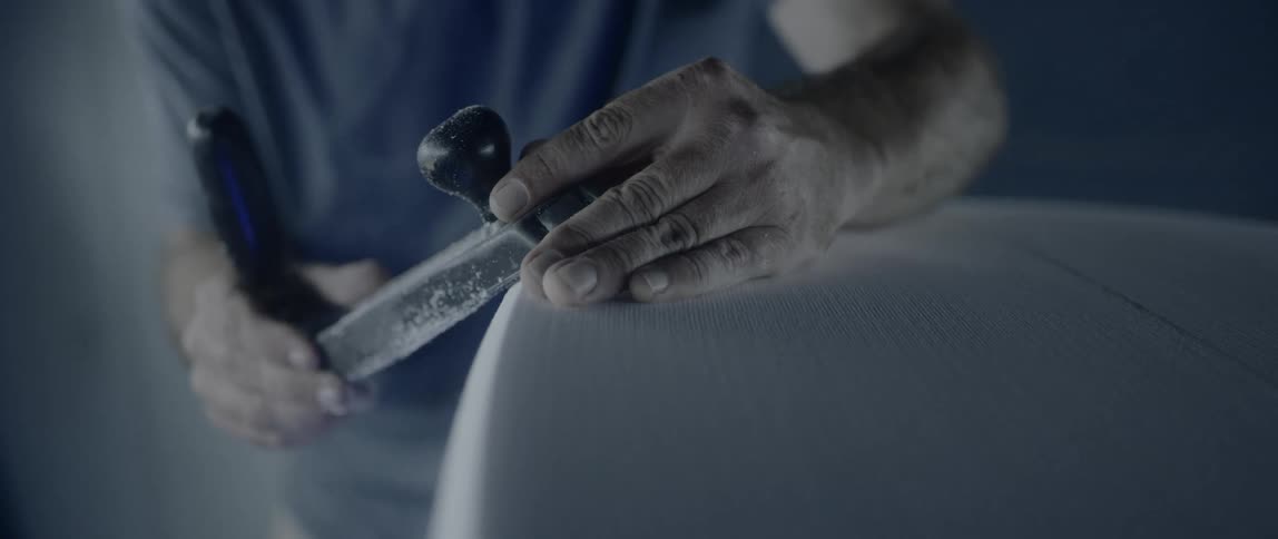 A white man uses a hand tool to sand the side of a surface