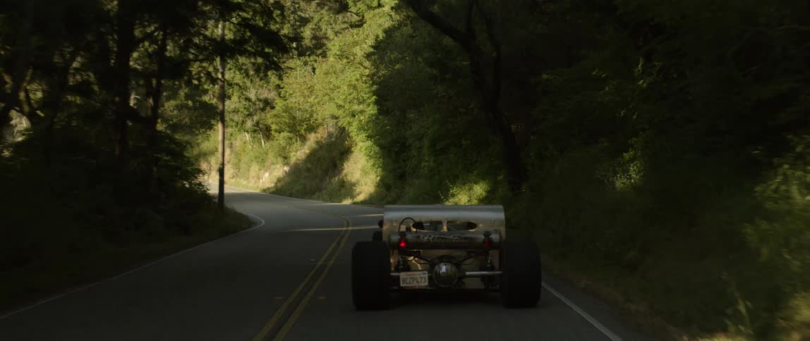 A vehicle driving on a road surrounded by grass and trees