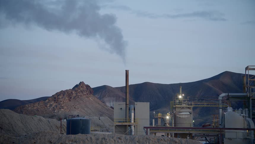 Smoke emits from the smoke stack in an industrial compound near the mountains