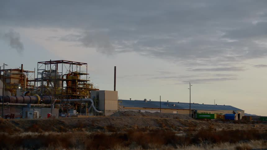 A road with a vehicle next to a refinery with chimneys and smoke