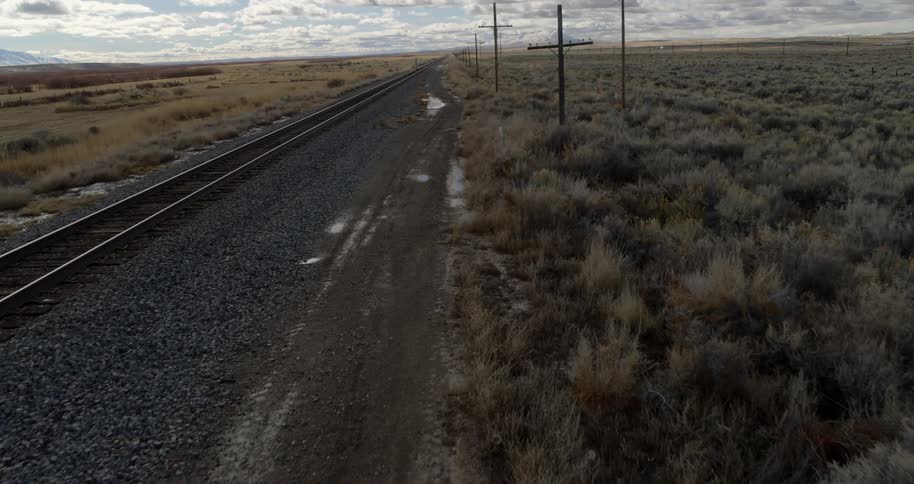 Railroad tracks run alongside a line of utility poles in a rural area