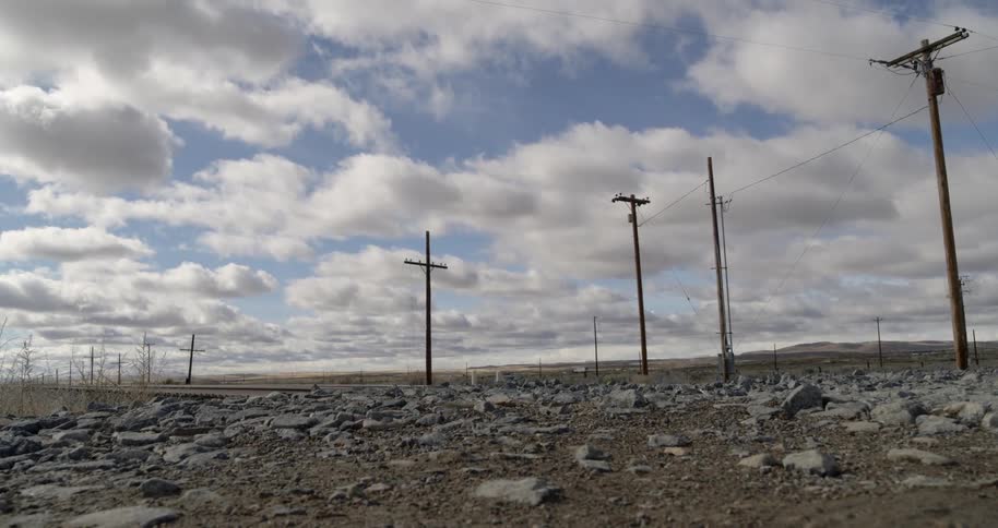 Telephone poles stand in a rocky barren landscape while cars and trucks travel on a road
