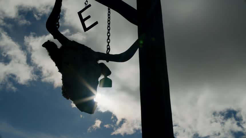 An animal skull hangs from a wooden crossbeam as storm clouds hover overhead