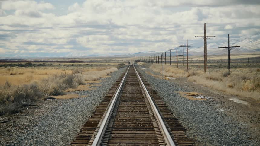 Train tracks run alongside power lines in a rural area