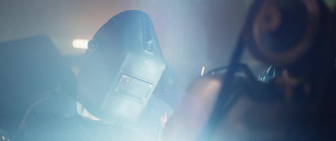 Man wearing welding helmet welds metal in a workshop