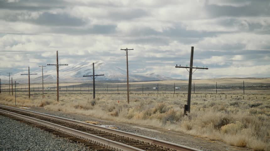 Train tracks next to a highway with mountains and the sky in the background
