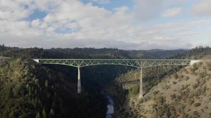 A tall bridge connects between two hills and over a narrow river
