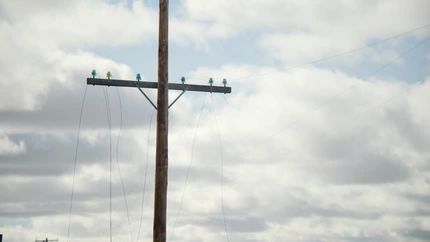 A tall wooden utility pole with broken wires in the field