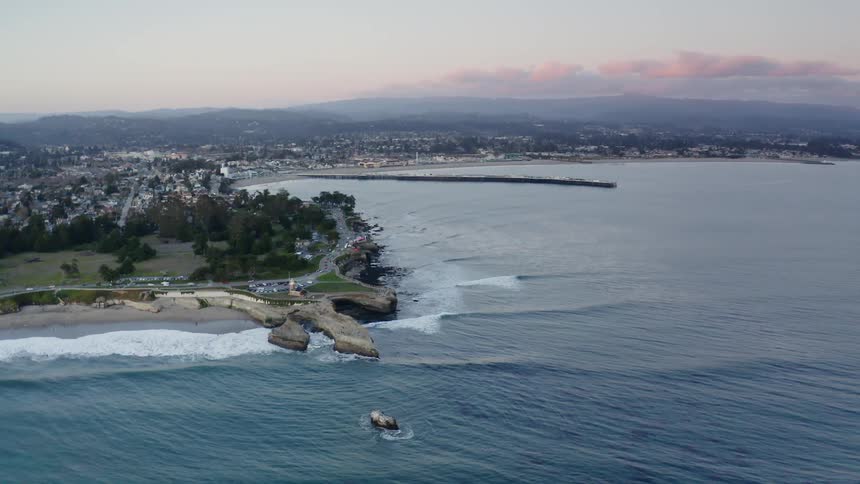 Aerial view of waves meeting the shore as cars drive on a street