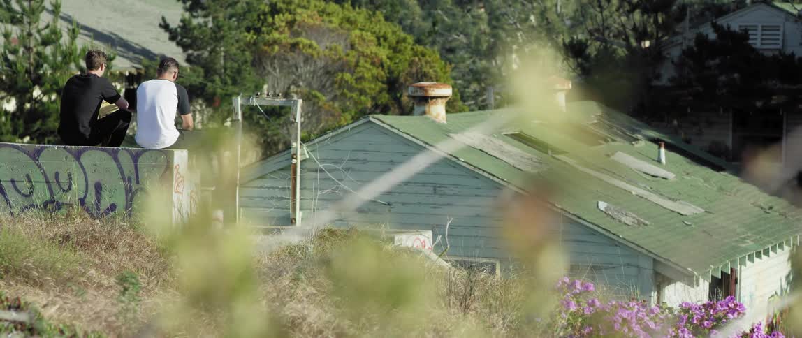 Two men sit on a ledge overlooking a building with a green roof