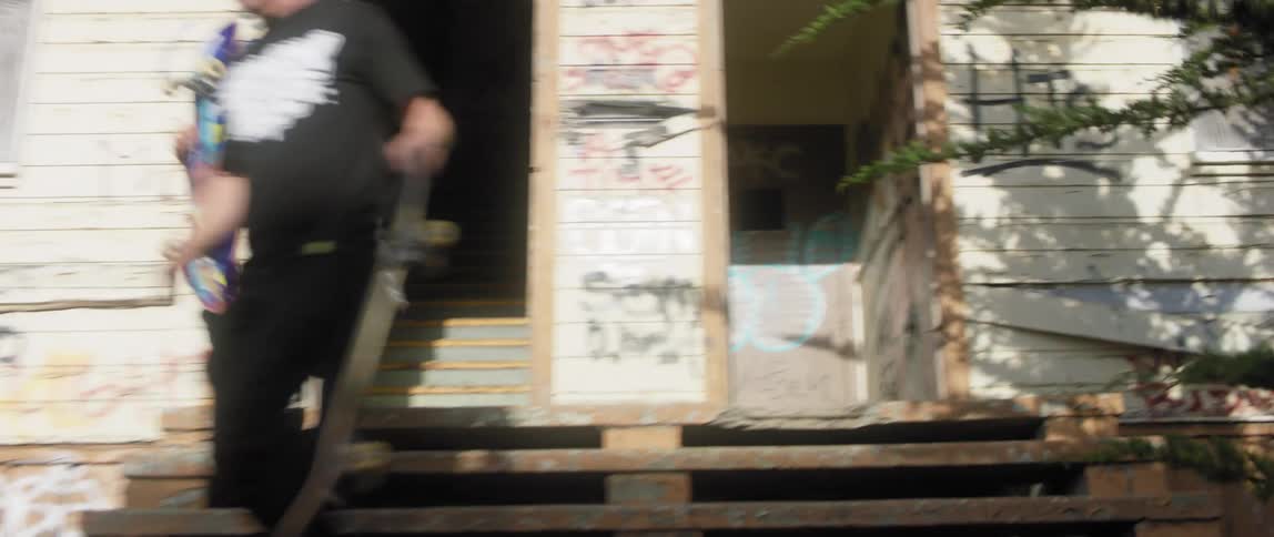 Two skateboarders get up and walk down the steps carrying their boards revealing a graffiti covered building and entrance