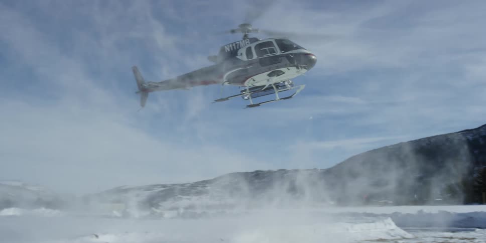 Helicopter flies toward snow covered ground stirring up snow near mountains