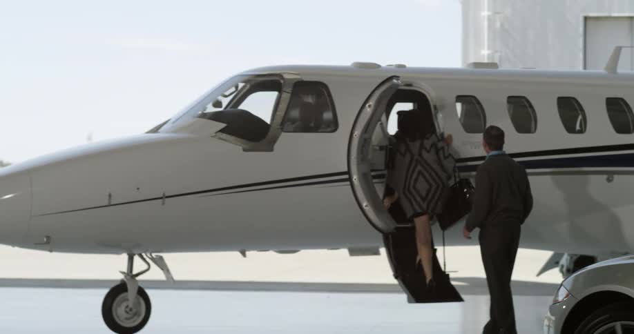 A man and a woman entering a private jet in a hangar at an airport during the day