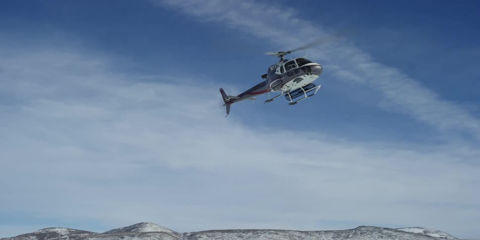 Helicopter with large blades comes down through the air onto the snowy ground