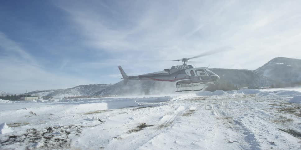 A helicopter lands on a stretch of ice with mountains in the background