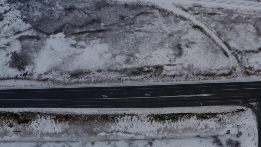 Cars drive along black asphalt highway that stands out against white snow covered countryside