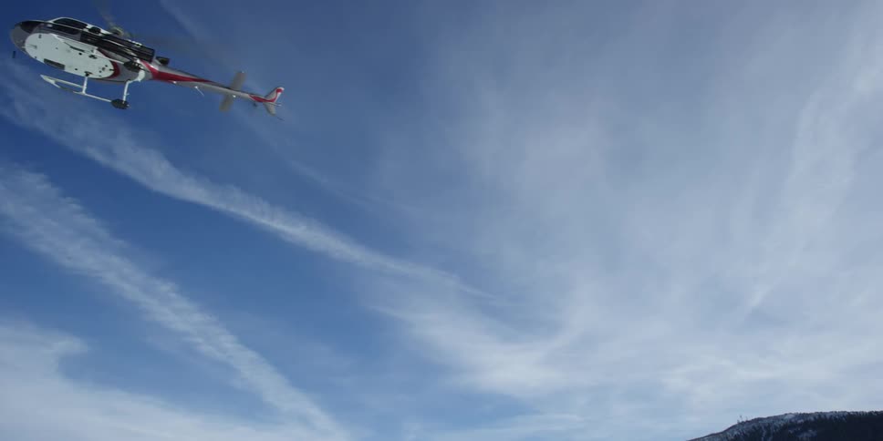 Helicopter with large blades flies overhead with clouds in the background