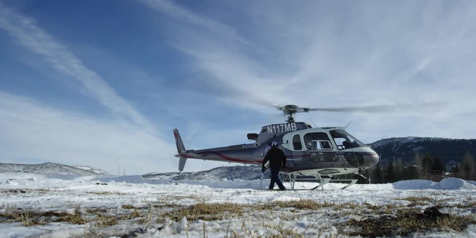 A helicopter pilot walks around and toward the back of a running helicopter