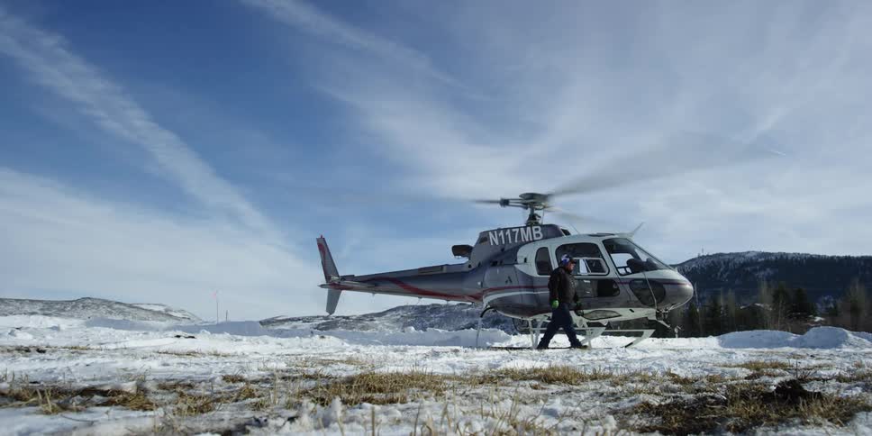A man walks away from a helicopter sitting in a snowy field