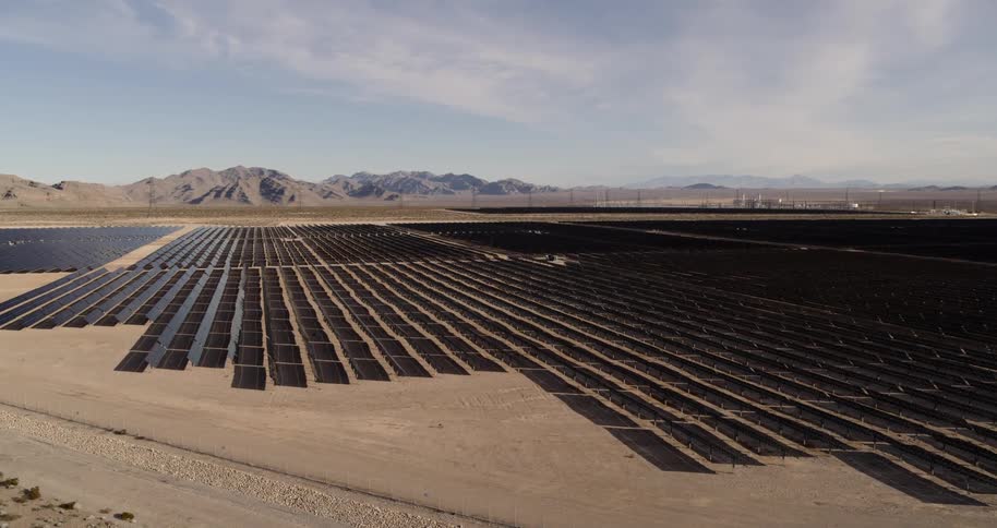 Many black solar panels sit in rows in the desert