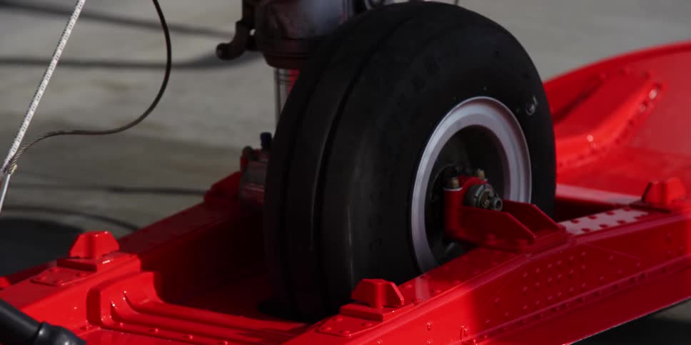 A shadow crosses over an aviation tire secured to a large red wheel lock