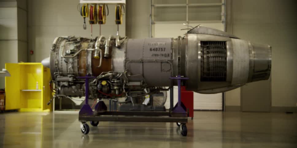 An engine sits on a cart in a clean workshop with a shiny floor