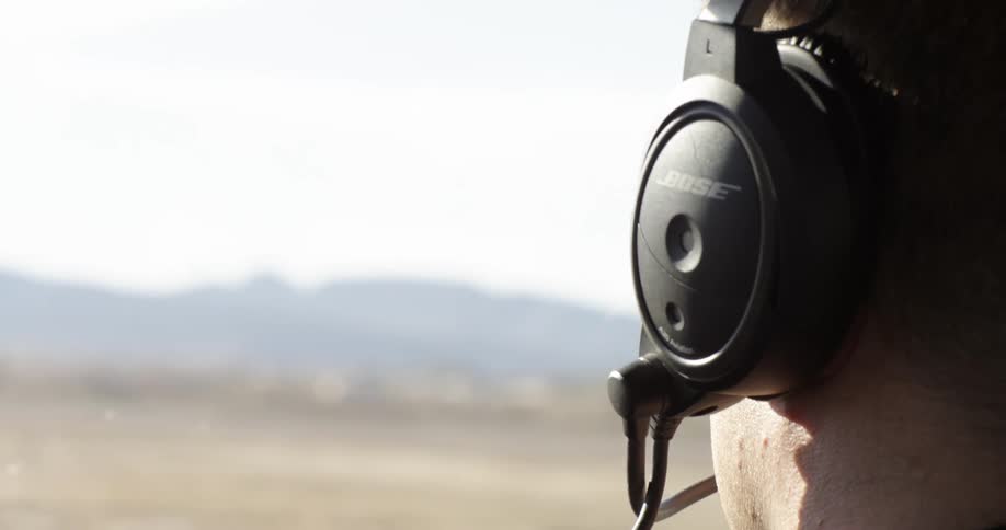 A man wearing headphones and a microphone stands in the desert on a windy day