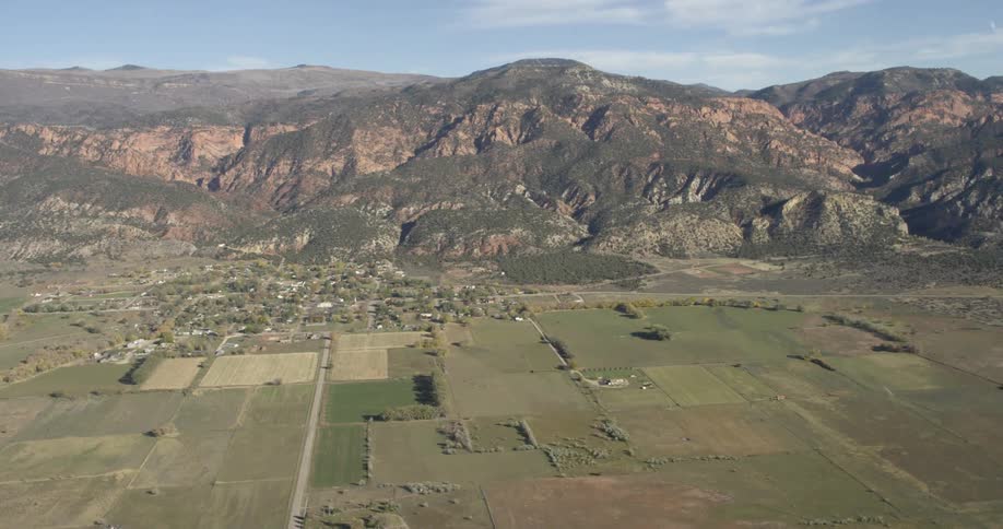 A neighborhood sits below a mountain range and is surrounded by flat plains