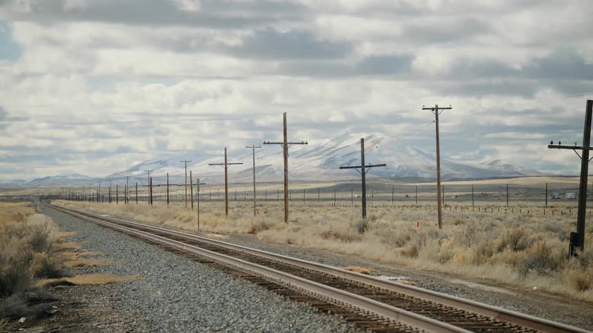 Train tracks and traffic run past a mountain range