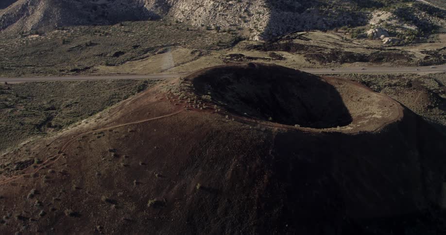 A road in the desert with vehicles next to a dormant volcano