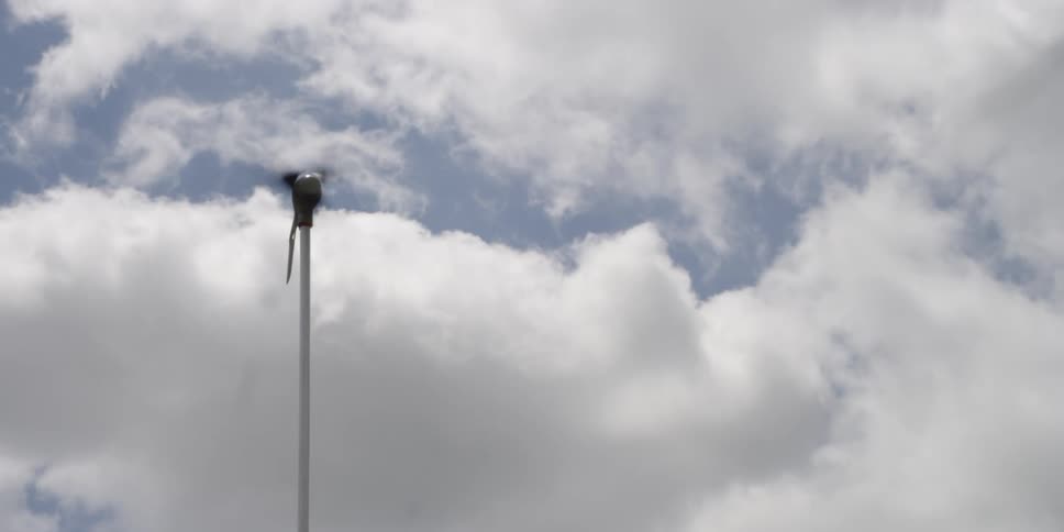 A small windmill turning in the wind with the sky and clouds in the background