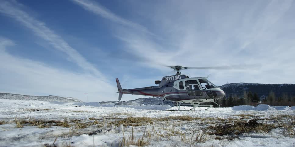 A helicopter with blades spinning sits in a snowy field