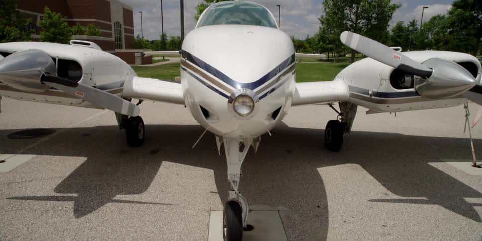 An airplane on the tarmac with grass and trees and a building in the background