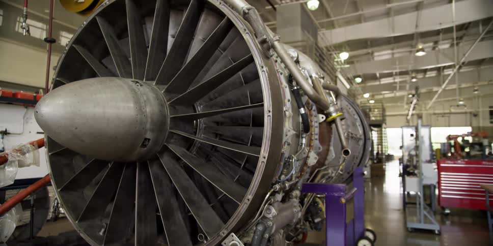 A large jet engine sits on a portable carts in a factory