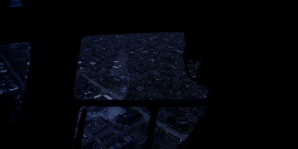 A man riding in the back of a helicopter looks out the window as it flies over a city