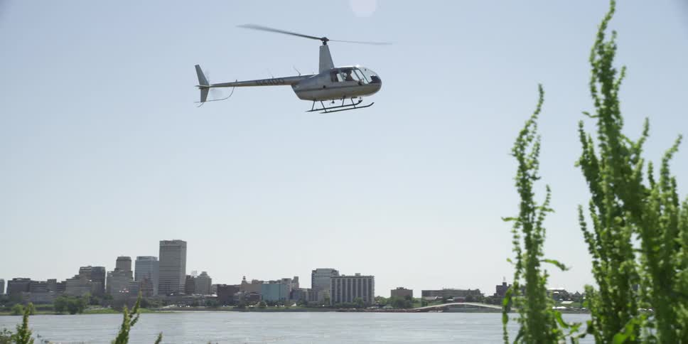 A helicopter flies over the coastline with the city skyline in the background